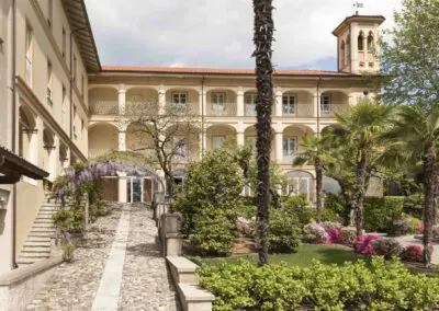 Casa Dei Padri retreat center with palm trees, flowers, and cobblestone path leading to the entrance