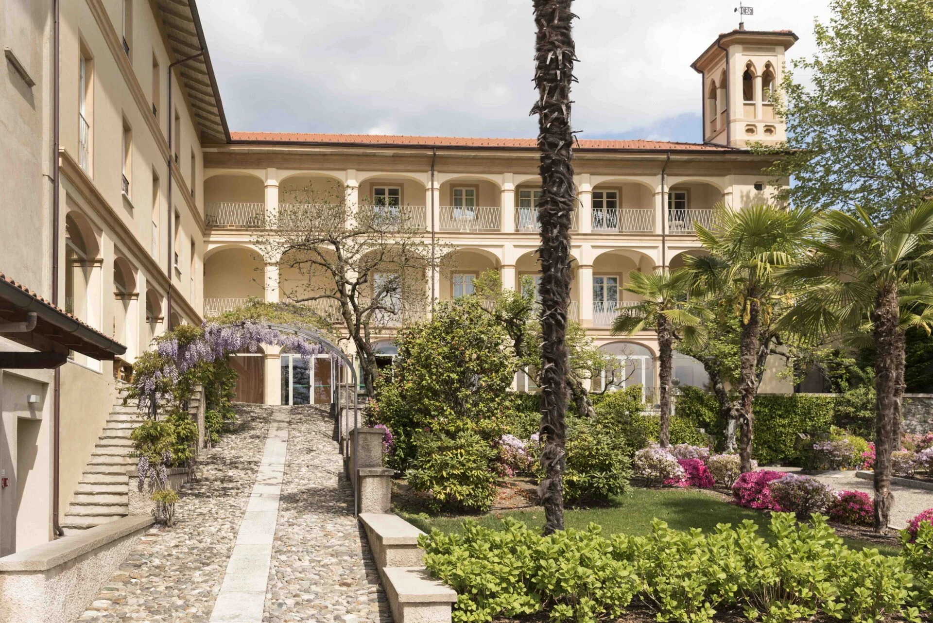 Casa Dei Padri retreat center with palm trees, flowers, and cobblestone path leading to the entrance