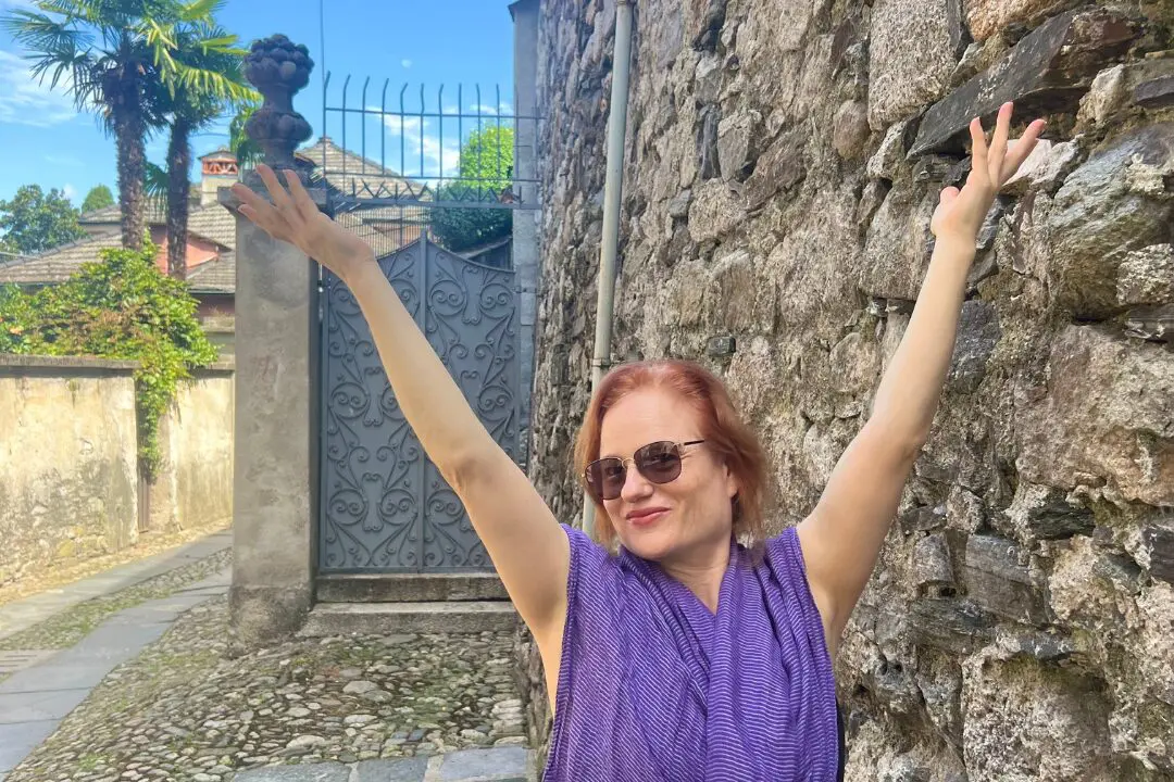 Stephanie Tack, somatic movement therapist, smiling with arms raised joyfully in a cobblestone alley in Italy