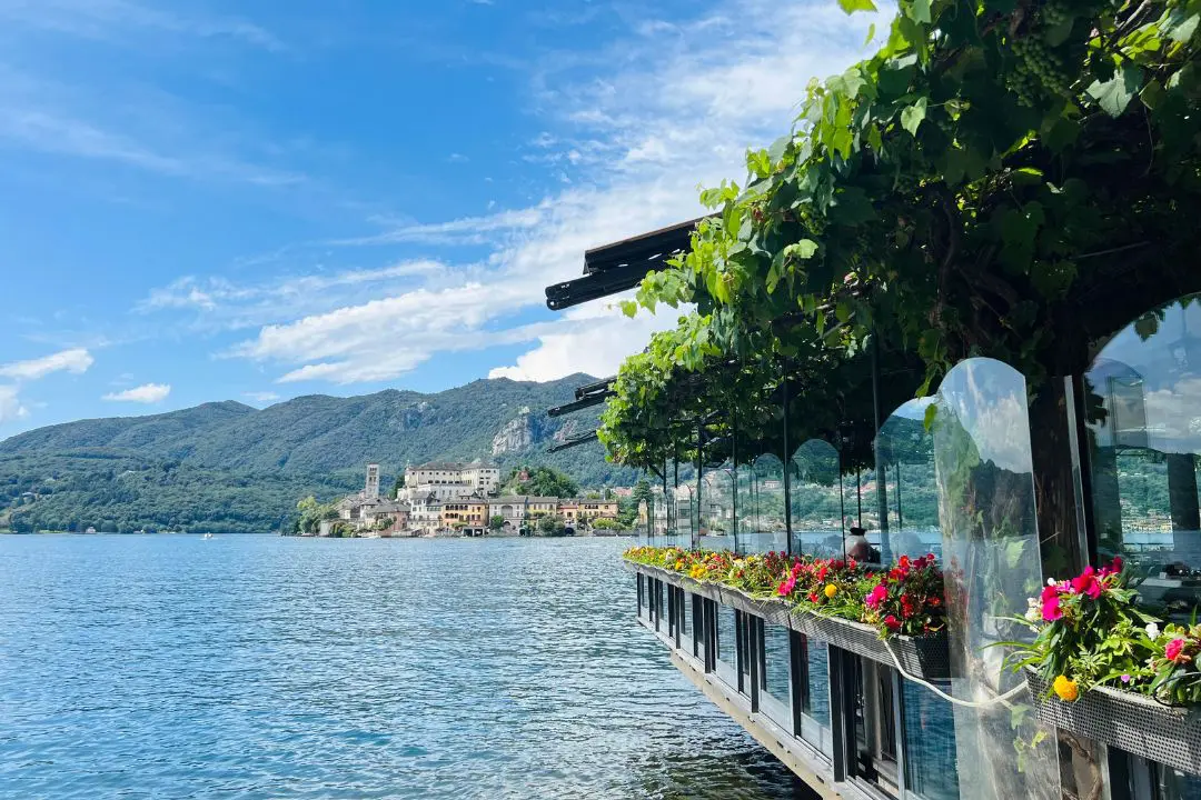 A lakeside restaurant in Orta with lush green vines and colorful flowers overlooking Isola San Giulio
