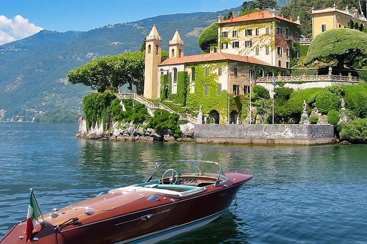 como-3-1 A vintage wooden boat anchored on the lake in front of an ivy-covered villa with mountains in the background during a retreat excursion in Italy