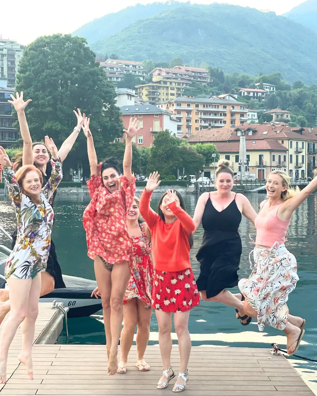 A joyful group of women jumping together on a dock at Lago d’Orta during the Goddess Yoga Retreat